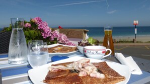 Una mesa con alimentos para el desayuno, una botella de agua, una jarra de cerveza y vista a la playa.