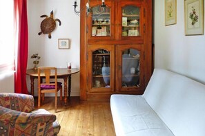 A cozy living room with a white sofa, a wooden cabinet with glass doors, a round wooden table with a chair, and a decorative turtle on the wall.