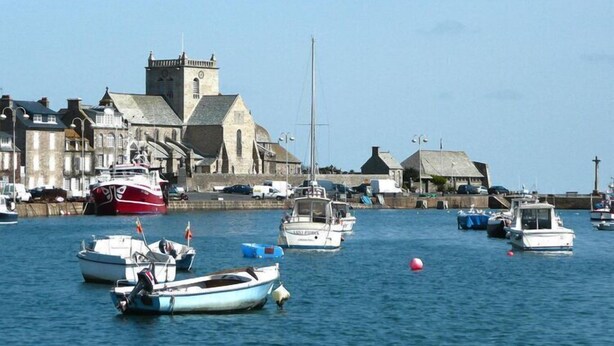 Un puerto con barcos amarrados, una iglesia y edificios a lo largo del paseo marítimo.