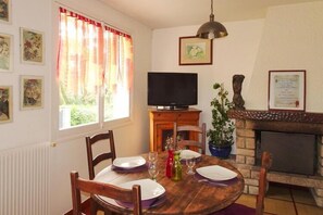 A dining area with a wooden table set for four, a television on a wooden stand, a fireplace, and framed certificates on the wall.