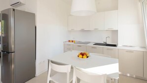Una cuina moderna amb armaris blancs, un frigorífic d'acer inoxidable, un menjador blanc amb dues cadires i un plat de fruita sobre la taula.