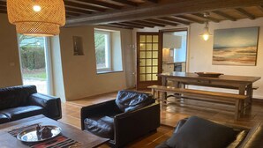 Ein Wohnzimmer mit einer Couch, einem Couchtisch, einem Esstisch mit einer Schüssel und Blick ins Freie durch ein Fenster.