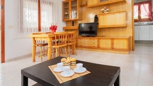 Moderni olohuone, jossa on puinen ruokapöytä, tuoleja, televisio sekä keittiöalue, jossa on kaappeja ja seinäkello.