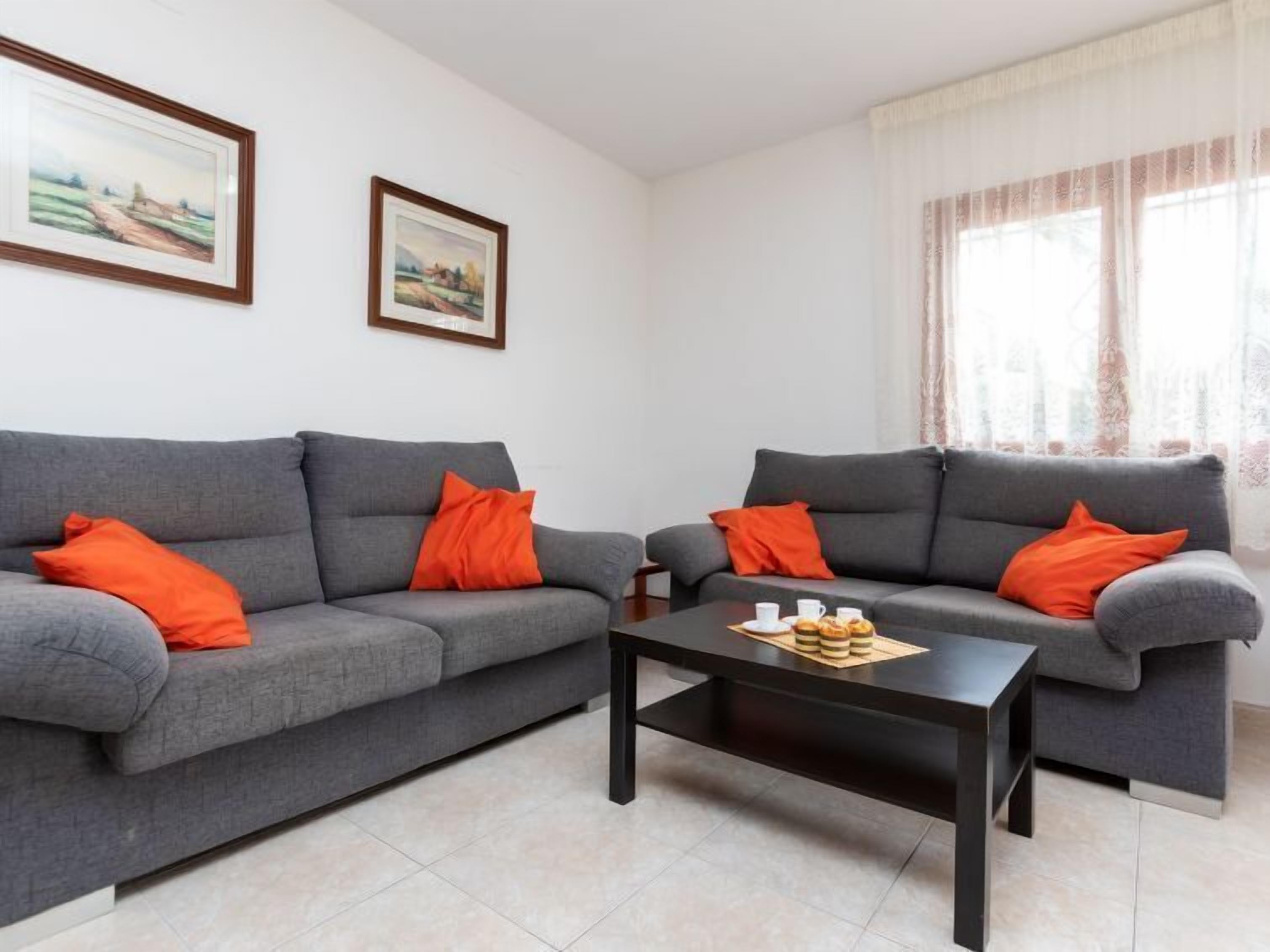 Una sala de estar con dos sofás grises, cada uno con una almohada naranja, una mesa de centro negra y dos cuadros enmarcados en la pared.