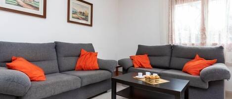 Una sala de estar con dos sofás grises, cada uno con una almohada naranja, una mesa de centro negra y dos cuadros enmarcados en la pared.