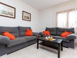 A living room with two grey sofas, each with an orange pillow, a black coffee table, and two framed pictures on the wall.