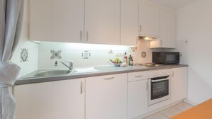 A kitchen with white cabinets, a sink, a microwave, and an oven. - Vissershuis 2 with parking by Interhome (De Haan)