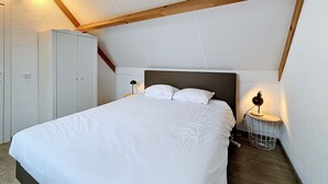 A bedroom with a bed, a wardrobe, a nightstand with a lamp, and a small round table with a lamp. - Vissershuis 2 with parking by Interhome (De Haan)