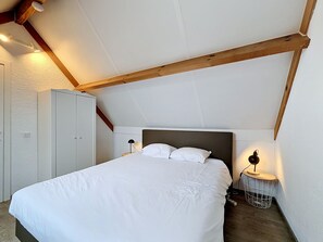 A bedroom with a bed, a wardrobe, a nightstand with a lamp, and a small round table with a lamp.