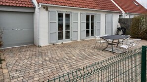 A house with a red-tiled roof, grey shutters, and a paved patio with a table and chairs. - Vissershuis 2 with parking by Interhome (De Haan)