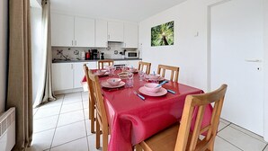 A dining area with a red tablecloth, wooden chairs, and a kitchen in the background. - Vissershuis 2 with parking by Interhome (De Haan)