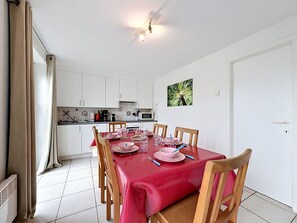 A dining area with a red tablecloth, wooden chairs, and a kitchen in the background.