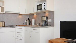 A modern kitchen with white cabinets, a microwave, a coffee maker, and a flat-screen TV on a wooden table. - Ferienwohnung, St. Peter-Ording (St. Peter-Ording)