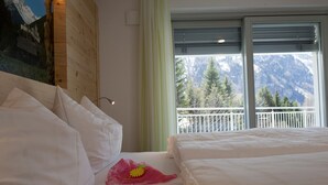 Quarto de hotel com duas camas, cabeceira de madeira, varanda com vista para a montanha e janela com persianas.