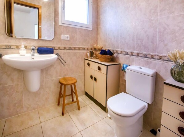 Un baño con lavamanos, inodoro y un taburete pequeño.