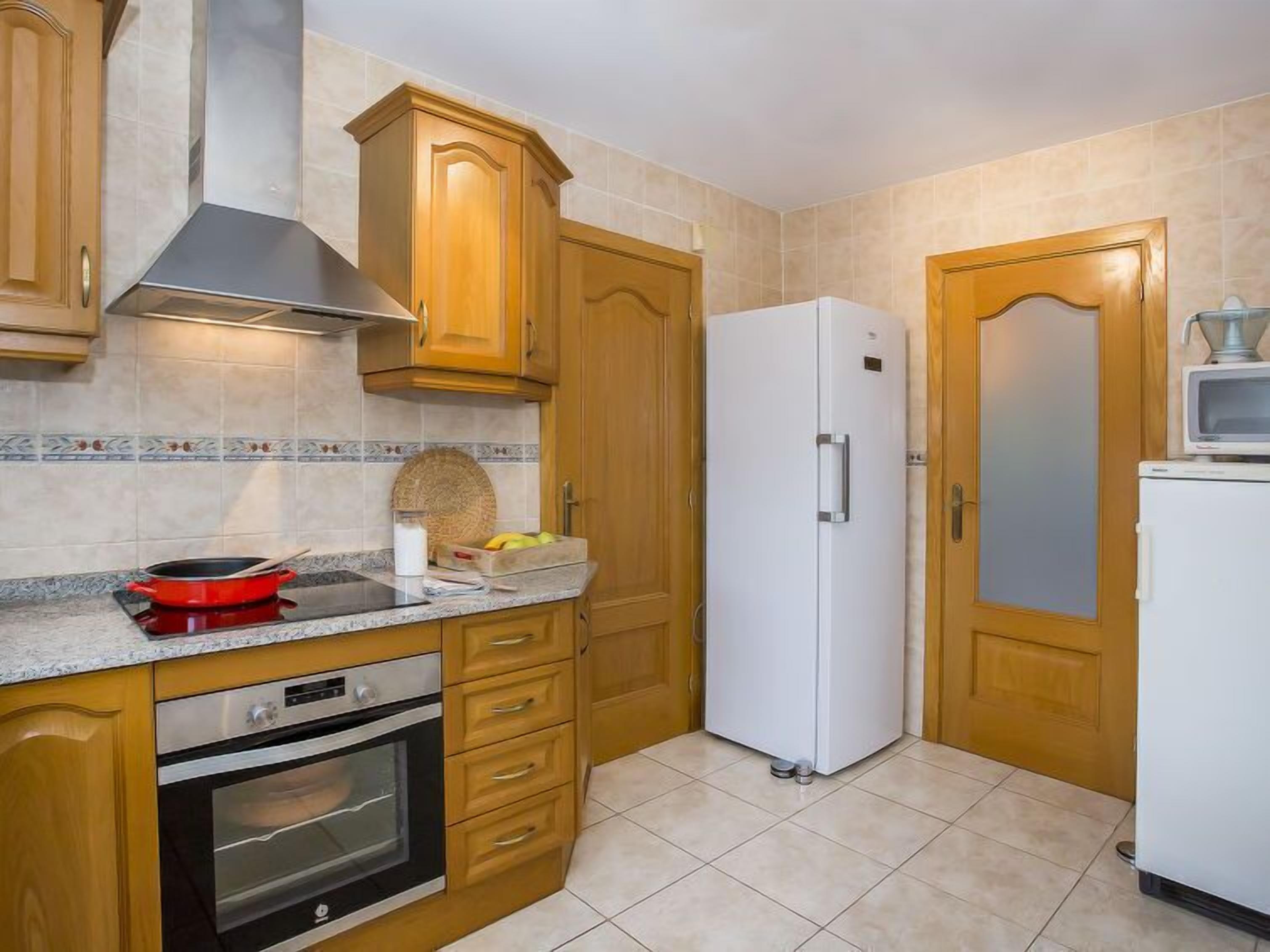 Eine Küche mit Holzschränken, einem weißen Kühlschrank, einer Mikrowelle auf dem Kühlschrank, einem Herd und einem Spülbecken.