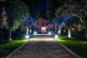 Un chemin menant à une maison à la façade rouge, entourée d’arbres et éclairée par de nombreuses sources de lumière.