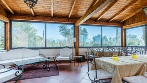 Un'ampia stanza con soffitto in legno, ampie finestre, un divano bianco, un tavolo da pranzo con sedie e una tovaglia fantasia.