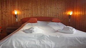 A neatly made bed with white linens and orange pillows, two wall-mounted lamps, and wooden paneling on the walls.