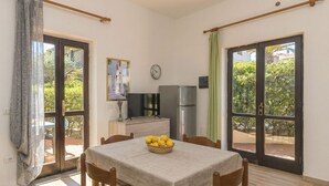 Zona pranzo con tavolo, sedie, frigorifero, televisore e finestra vista sul verde.