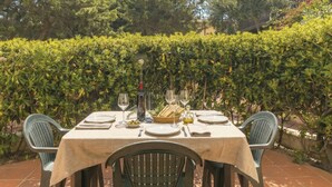 Zona pranzo all'aperto con un tavolo apparecchiato per due, circondata da vegetazione e un edificio sullo sfondo.