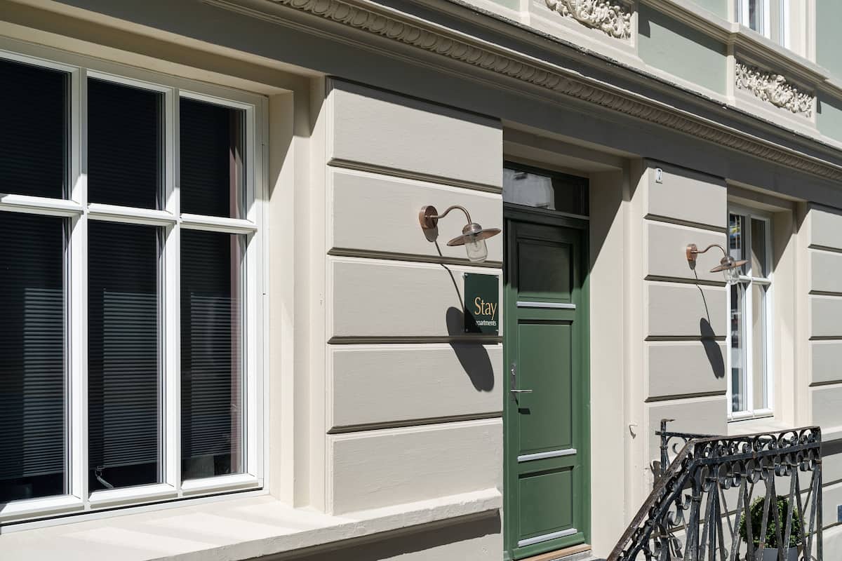 Een gebouw met een groene deur, witte luiken en een bord waarop 'Stay' staat.