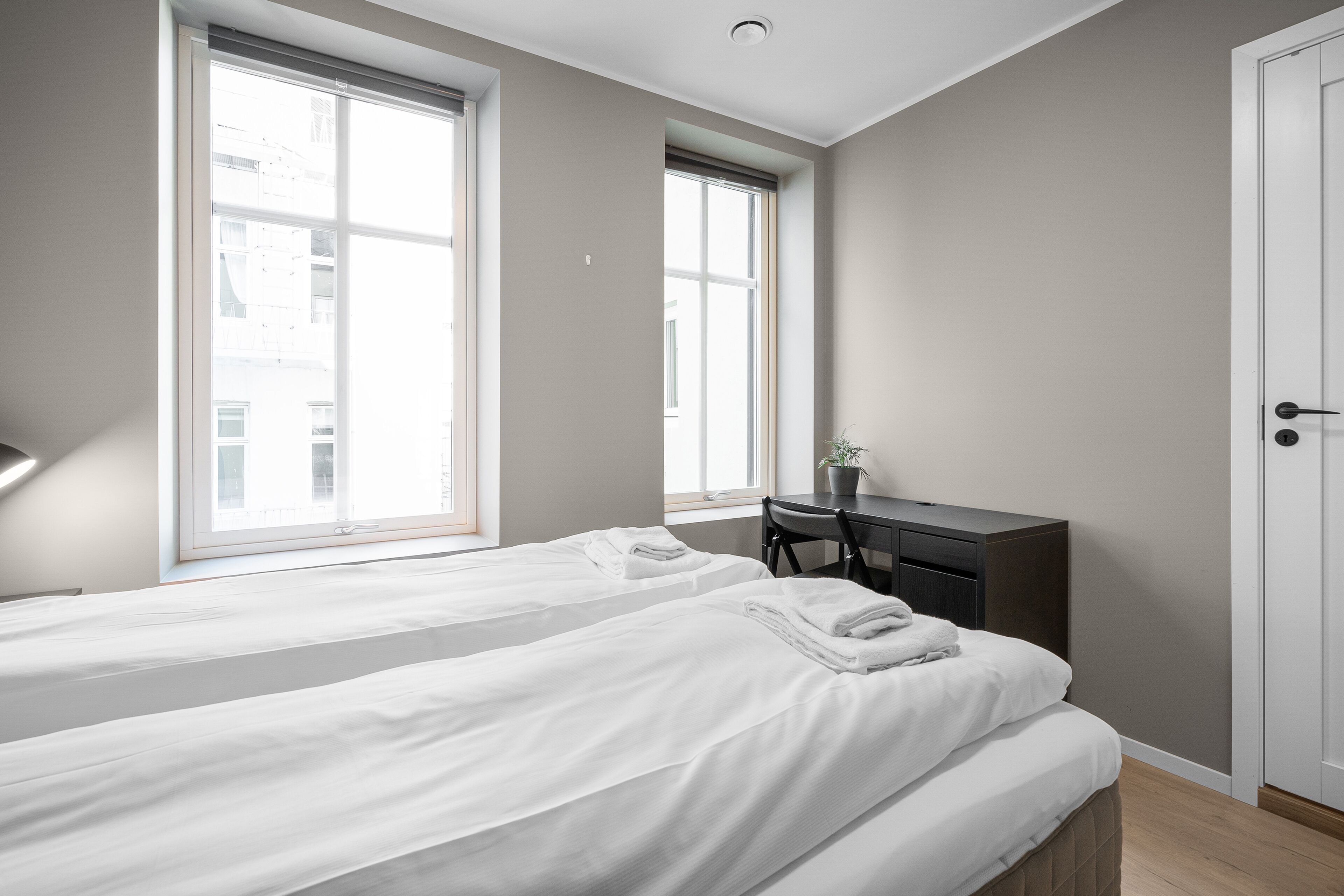 A bedroom with two beds, a desk, and a door.