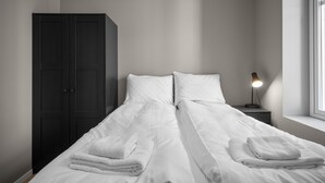 Ein Schlafzimmer mit einem Bett, zwei Kissen, einem Nachttisch mit Lampe, einem Kleiderschrank und einem Fenster.