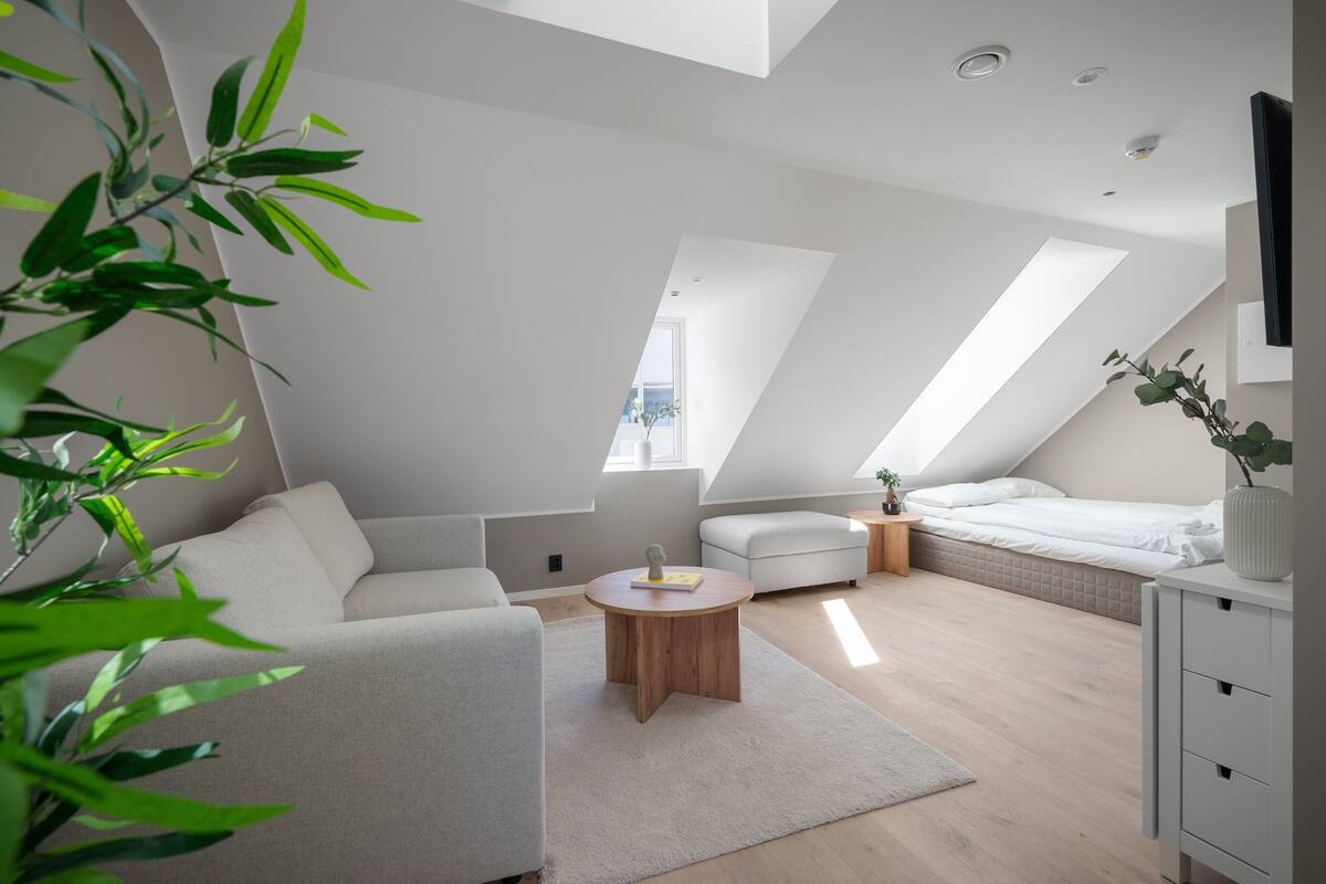Een moderne loft slaapkamer met een schuine plafond, een bank, een bed, een nachtkastje en een kleine ronde houten tafel.
