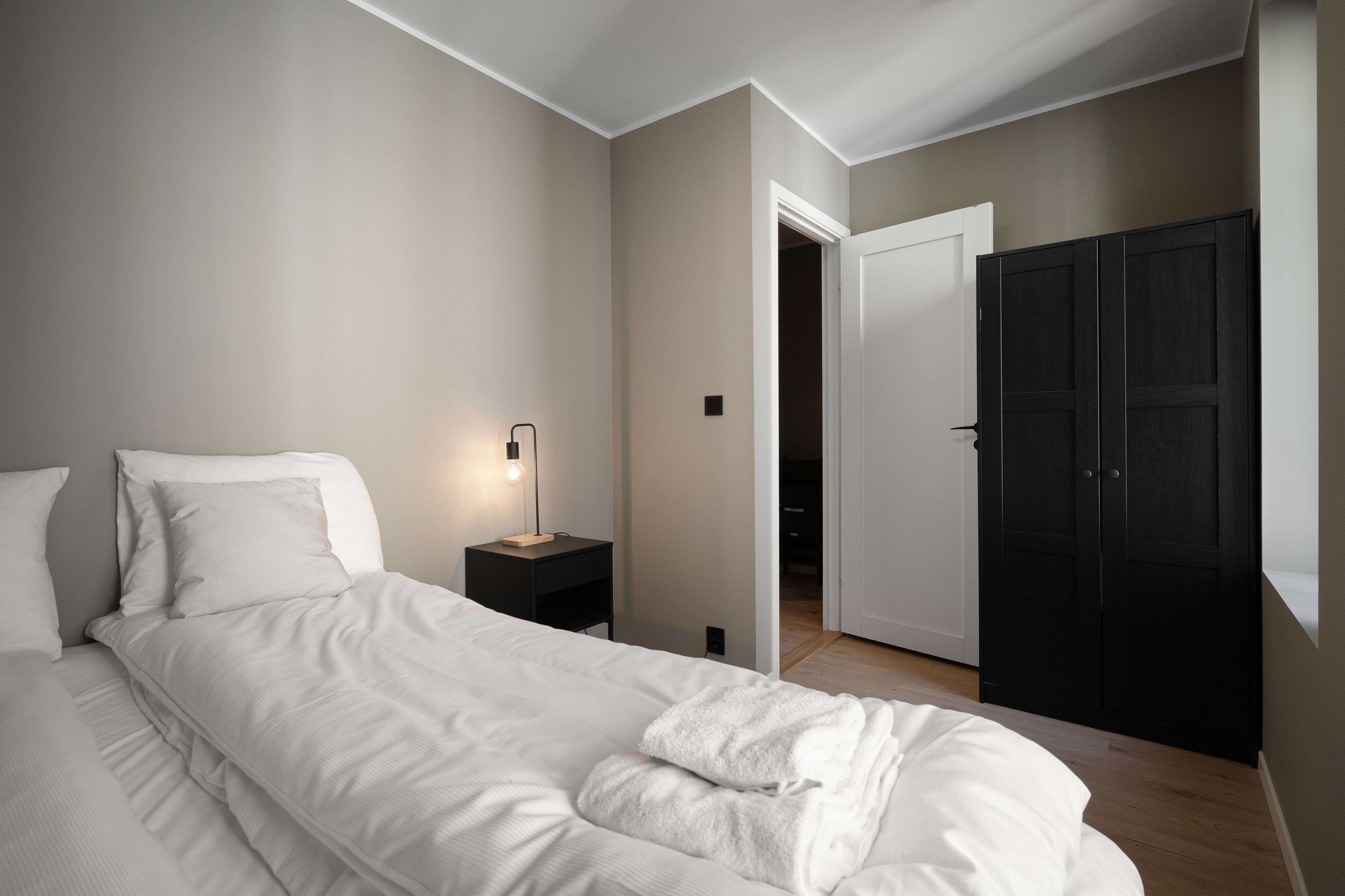 A bedroom with a bed, bedside table, lamp, and wardrobe.