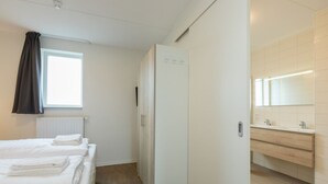 Een hotelkamer met twee bedden, een raam met gordijnen, een witte kledingkast en een badkamer met een spiegel en wastafel.