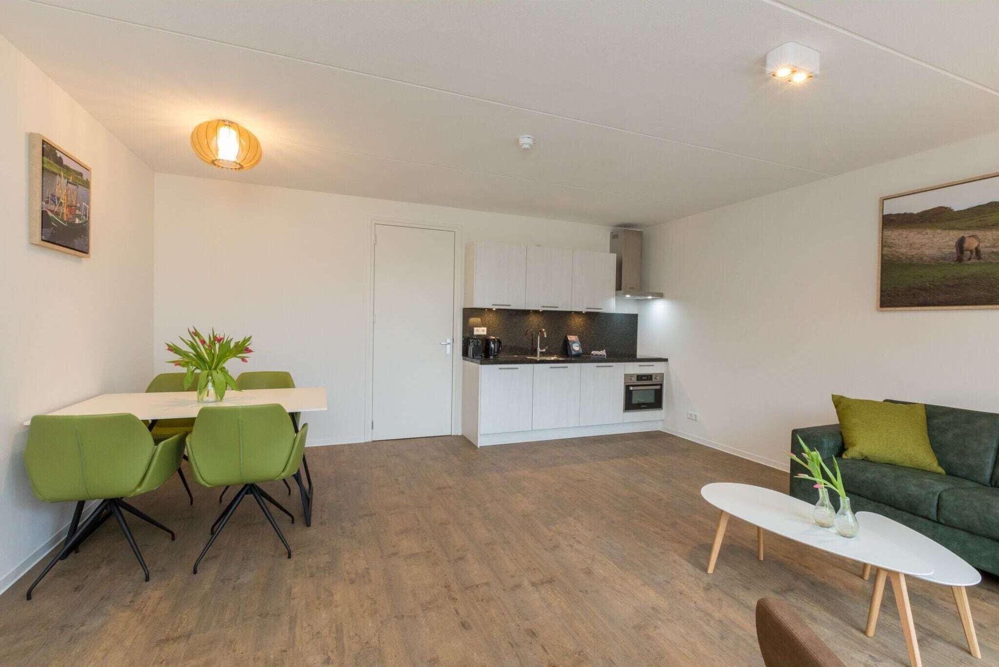 Un espace de vie moderne et compact, comprenant un coin repas, une kitchenette et un canapé vert.
