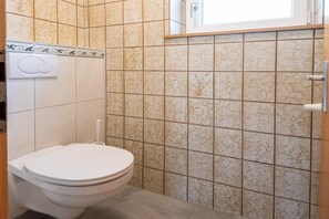 Ein Badezimmer mit Toilette, Handtrockner und gefliesten Wänden.