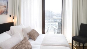 A hotel room with a large bed, a chair, a painting on the wall, and a view of the city through the window. - Apartment in Netherlands near the Beach (Den Haag)