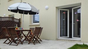 An outdoor patio with a table and chairs, a large umbrella, and a sliding glass door with butterfly decals. - House in Saint-Quay near 7 Beaches (St. Quay-Portrieux)