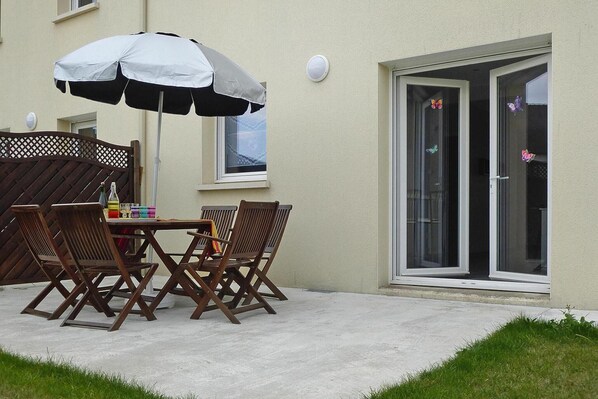 An outdoor patio with a table and chairs, a large umbrella, and a sliding glass door with butterfly decals.