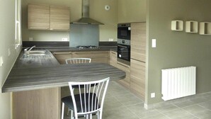 A modern kitchen with a central island, built-in oven, and stainless steel appliances. - House in Saint-Quay near 7 Beaches (St. Quay-Portrieux)