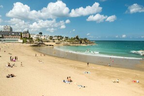 A beach with people sunbathing and swimming. There are buildings in the background.