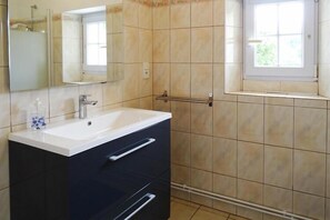 Bathroom features a large sink, mirror, and towel rack, with a window offering a view of the surrounding greenery.