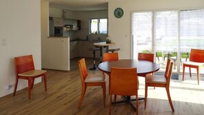 Comedor con mesa redonda y seis sillas, cocina al fondo y vista a través de una puerta de vidrio.