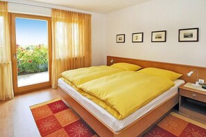 A hotel room with a large bed, a nightstand, a window with curtains, and a view of greenery outside. - Apartment in Schlanders near Stelvio Park (Schlanders)