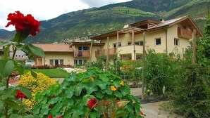 Um edifício de dois andares com varanda, rodeado por vegetação exuberante e montanhas ao fundo.