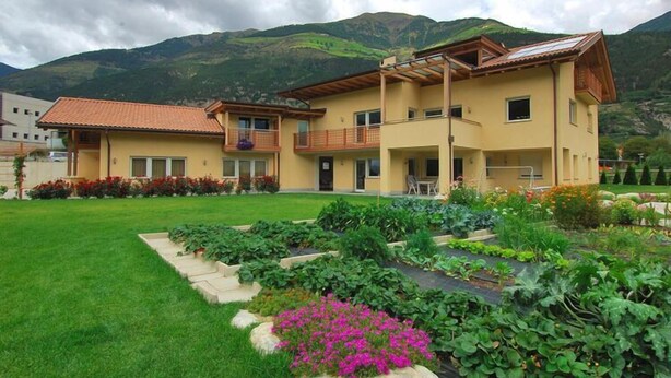Um edifício de dois andares com varanda e jardim à frente.