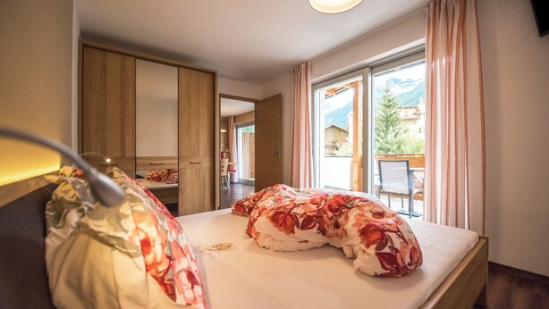 Un dormitorio con cama, mesita de noche, lámpara, ventana con cortinas y vistas al exterior.