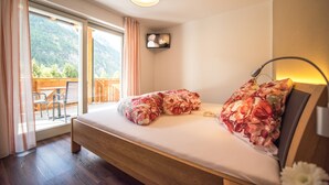 Un dormitorio con cama, mesita de noche, lámpara, ventana con cortinas y vistas al exterior.