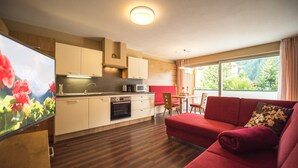Una cocina moderna con armarios blancos, un área de comedor con un sofá rojo y un ventanal con vistas a zonas verdes.