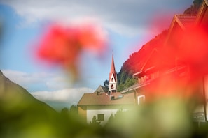 A church with a steeple, surrounded by greenery and a mountain backdrop.