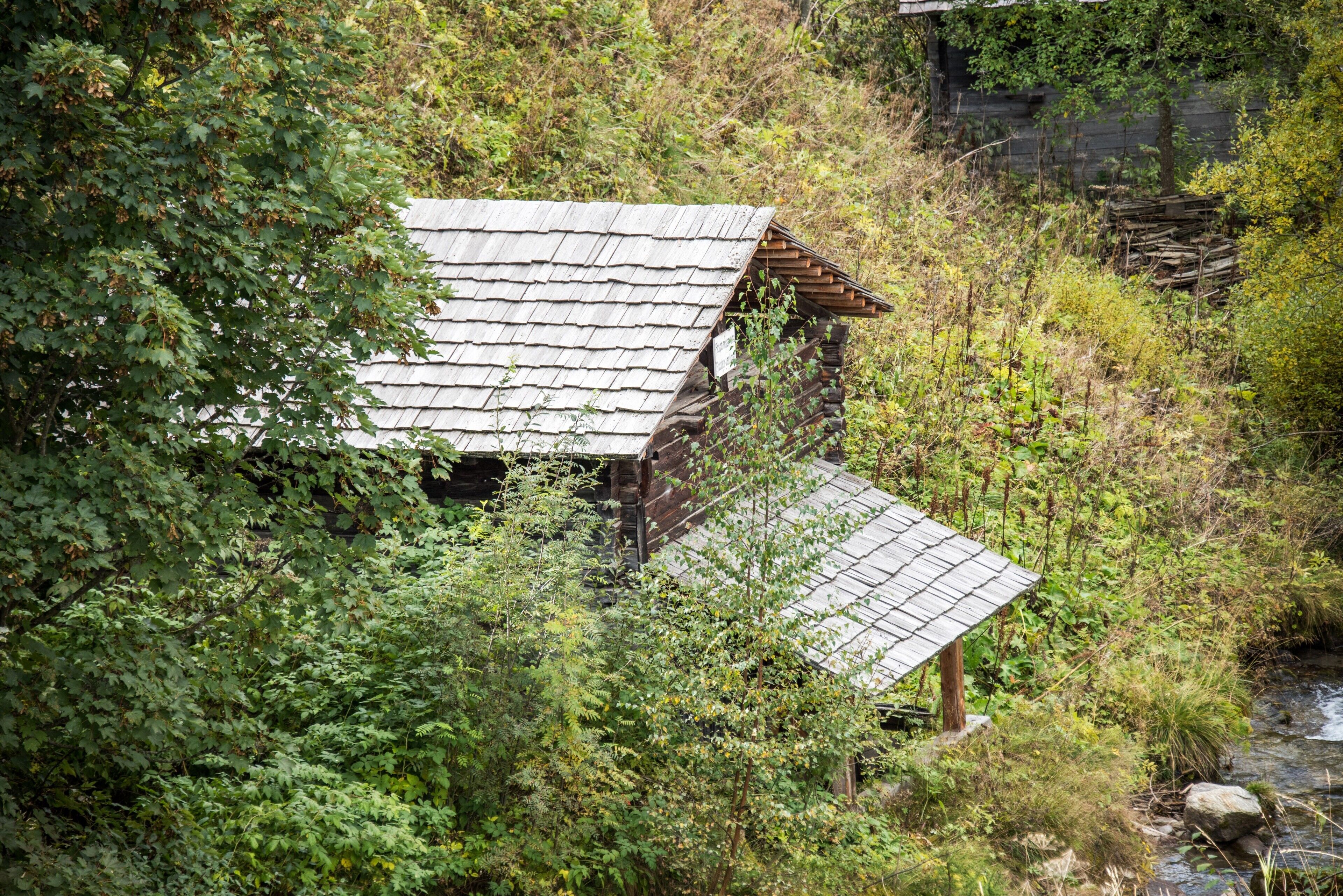Un rustico chalet in legno con tetto spiovente, immerso nel verde e con un ruscello nelle vicinanze.