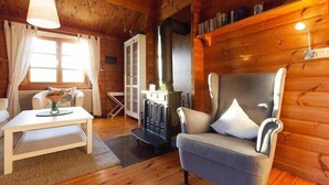 Een gezellig interieur van een chalet met een bank, een tafel met een vaas, een open haard en houten wanden.