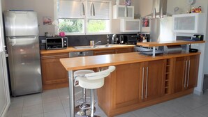 A modern kitchen with stainless steel appliances, wooden cabinetry, and a central island with bar stools. - Holiday Home in Crozon near Sandy Beaches (Crozon)
